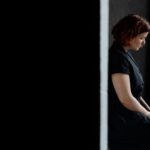 A woman in a black dress sits contemplatively beside a concrete wall, offering ample copy space.
