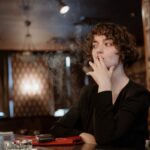 A woman sitting at a table inside a cozy cafe, thoughtfully smoking.